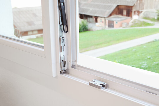 Tilt-and-turn window hardware. Close up of white uPVC window mechanism with pivot gear, locking tongue, and keeper strike plate. Repair and maintain or installation service. Selective focus.