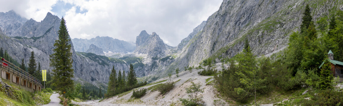 Panoramic view of H&ouml;llental valley and alpine mountain range near Zugspitze in Grainau, Bavaria, Germany. High mountain peaks, rocky slopes, pine trees, and hiking infrastructure in summer.