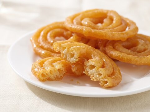 Indian jalebi sweets broken open on a white plate, traditional Indian dessert, crispy texture, syrup soaked pastry interior, golden fried spirals, close up food photography