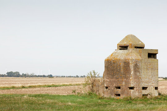 Abandoned Concrete Pillbox Bunker on Coastal Field With Wind Turbines on Horizon