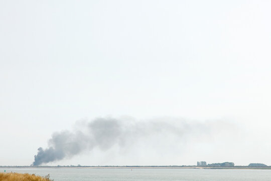 Distant Smoke Plume Over Coastal Waterline With Low Horizon and Hazy Overcast Sky