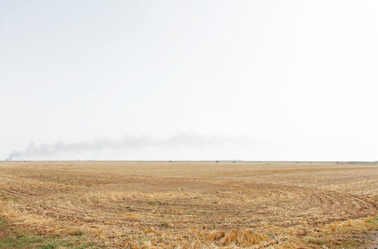 Dry Harvested Farmland Under Wide Sky With Distant Smoke on the Horizon