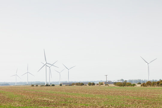 Wind Farm In Rural Farmland With Turbines Generating Renewable Energy On A Calm Overcast Day