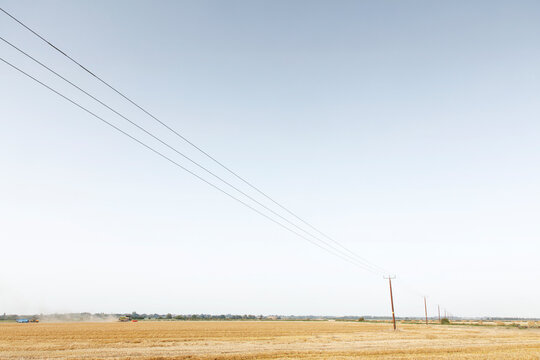 Power Lines Stretching Over Golden Harvest Field Under Clear Blue Sky in Rural Countryside