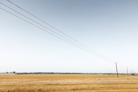 Rural Harvest Field With Tractor and Power Lines Stretching Across a Golden Countryside Landscape