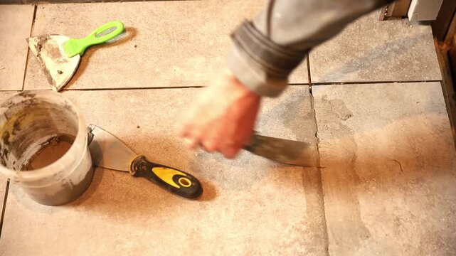 Worker applying grout with a putty knife between floor tiles. Bathroom renovation and tile installation