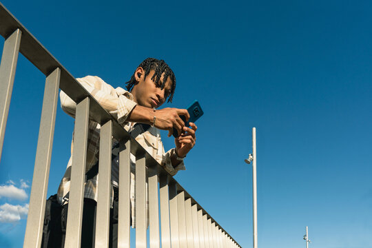 Young man using smartphone while leaning on railing