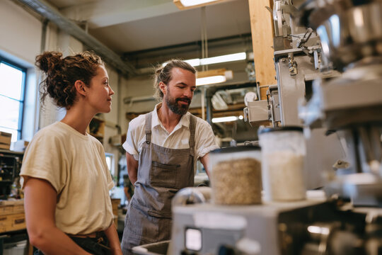 A woman and a man engage in conversation in a well-designed workspace filled with equipment and tools used for food preparation, illustrating collaboration and creativity.