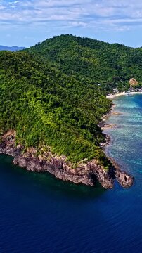 Aerial view of Port Barton Beach with lush green hills, rocky cliffs, and turquoise waters in Mimaropa, Philippines.