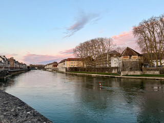 Flusslandschaft bei Dämmerung: ruhiges Wasser spiegelt rosa-rote Wolkenszenerie. Rechts historische Steinmauer mit Turm und kahlen Bäumen, links Altstadtbebauung.  kühle Jahreszeit, sanftes Licht. © Thomas