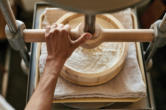 An overhead view of a hand operating a traditional flour sifter or mill, capturing the process of milling flour and the textures involved in creating ingredients for cooking.