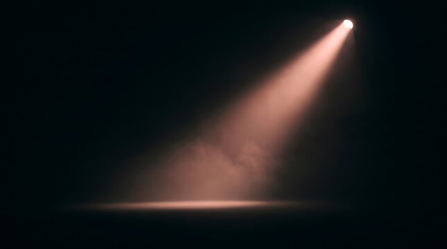 A single bright spotlight beam shining down onto a dark stage floor, creating a dramatic atmosphere with swirling haze and soft illumination in a theater or studio setting