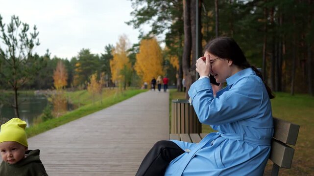 Worried Woman Talks On Cell Phone As Little Toddler Wanders Along Wooden Path In Autumn Park, Displaying Rising Stress While Distracted Parent Eventually Notices Missing Child And Looks Up.