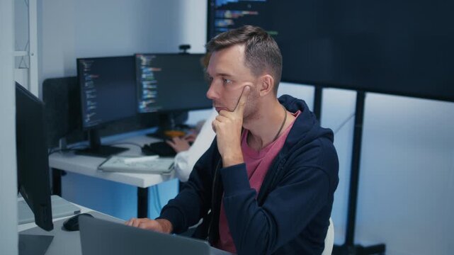 Professional Male Programmer Wearing Glasses Reviewing Source Code and Investigating Technical Problems During Focused Work Session. Programmer Reviewing Computer Code with Concentrated Expression.