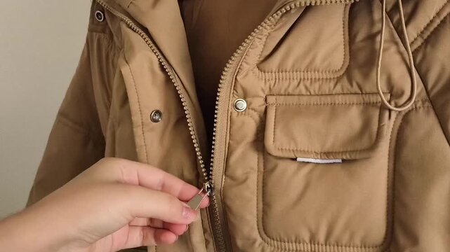 Close-up of a woman zipping up a padded winter jacket on a hanger at home, highlighting garment maintenance, practical clothing care, and seasonal wardrobe preparation.