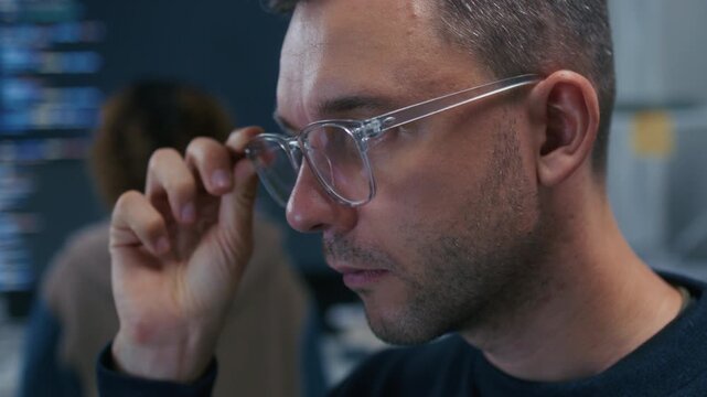 Professional Male Programmer Wearing Glasses Reviewing Source Code and Investigating Technical Problems During Focused Work Session. Programmer Reviewing Computer Code with Concentrated Expression.