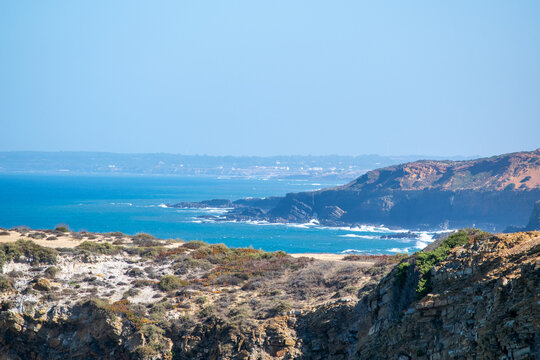 Dramatic coastal landscape with rugged cliffs, turquoise ocean, and distant cityscape under a clear sky