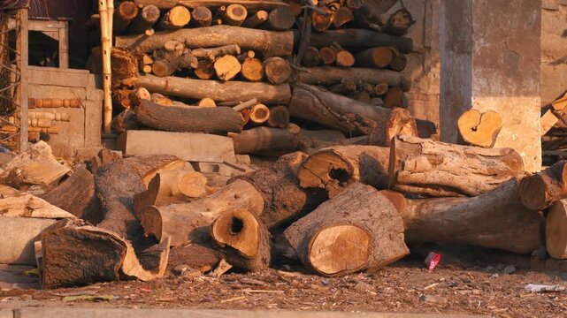 Cinematic wide static shot of firewood logs neatly piled and scattered on the ground for funeral pyres at the cremation grounds along the Ganges River in Varanasi, Uttar Pradesh, India.