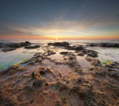 Beautiful rocky sea coast under vibrant sunset sky with long exposure smooth water effect. Twilight ocean shore landscape