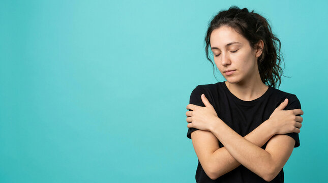 Young woman embracing herself with closed eyes, symbolizing self-comfort and introspection, highlighting Mental Health's vital role in well-being