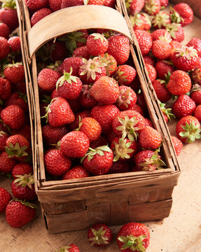 Fresh ripe strawberries in a wooden basket with scattered berries