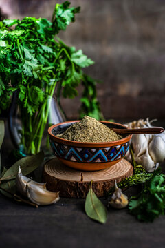 Powdered utskho suneli spice in a ceramic bowl with garlic cloves