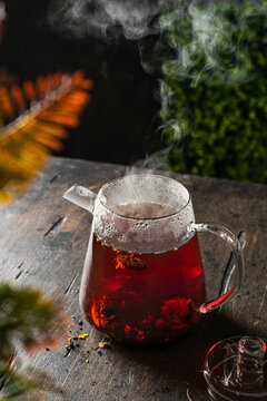 Steaming hot hibiscus tea in glass teapot on wooden table