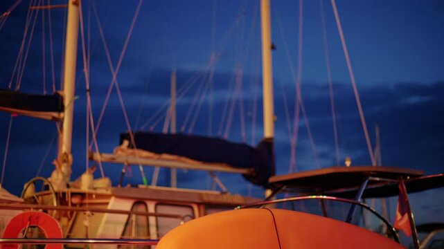 Orange paddle board on a boat deck in front of a classic sailboat with masts, rigging and a lifebuoy under a deep blue evening sky, French Riviera, France.