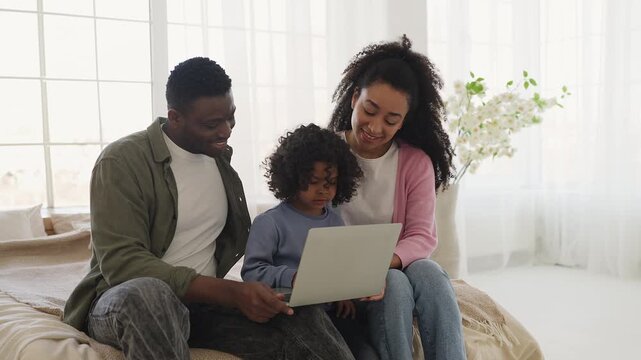 Little African American boy and parents play educational game on laptop