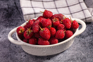 Checkered kitchen towel behind ripe red raspberries piled in white ceramic serving dish on dark stone surface, summer berry harvest © Andrei Starostin