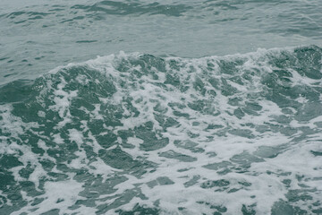 A high-angle close-up shot capturing the dynamic movement of deep turquoise sea water creating churned white sea foam and splashing wave ripples, perfect for background texture or marine life themes. © Teerawut