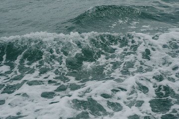 A high-angle close-up shot capturing the dynamic movement of deep turquoise sea water creating churned white sea foam and splashing wave ripples, perfect for background texture or marine life themes. © Teerawut