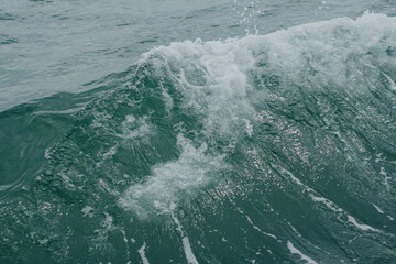 A high-angle close-up shot capturing the dynamic movement of deep turquoise sea water creating churned white sea foam and splashing wave ripples, perfect for background texture or marine life themes. © Teerawut