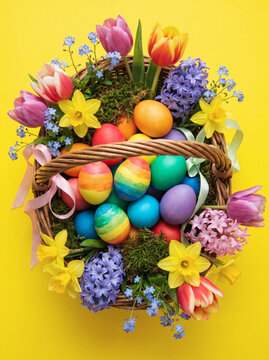 easter wicker basket with colorful eggs and spring flowers on bright yellow background vertical holiday still life for spring celebrations and greetings