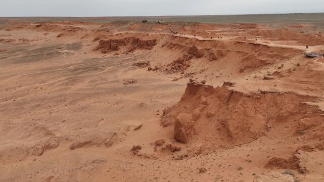 Cinematic drone perspective above the wind-sculpted badlands, red clay hills, and expansive arid landscape of the Flaming Cliffs in Mongolia