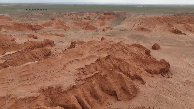 High angle drone view panning across the iconic red sandstone cliffs, geological layers, and rugged badlands of the Flaming Cliffs in the Gobi Desert