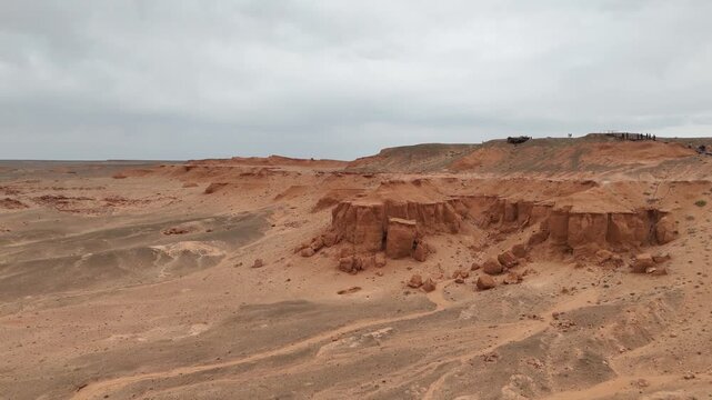 drone view across the iconic red sandstone cliffs, geological layers, and rugged badlands of the Flaming Cliffs in the Gobi Desert