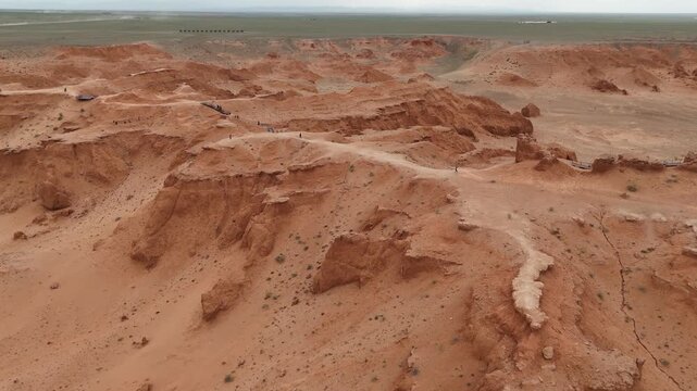 Cinematic aerial drone shot tracking across the dramatic red clay canyons, steep eroded slopes, and badlands of the Flaming Cliffs in Mongolia