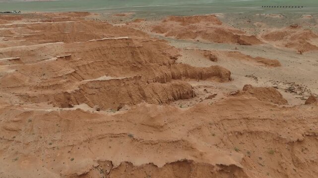 Sweeping drone view over the rugged red sandstone cliffs and wind-carved geological formations of the Flaming Cliffs in the Gobi Desert, Mongolia.