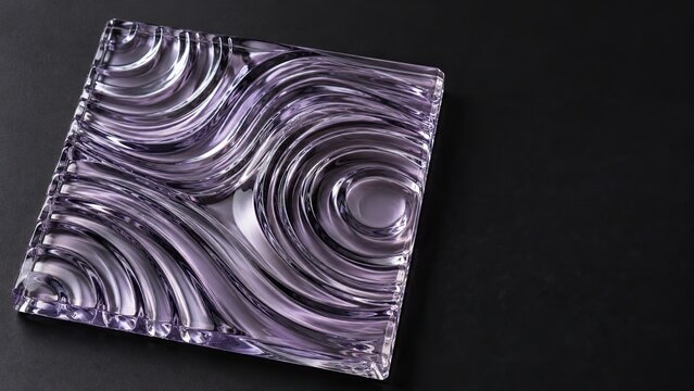Abstract stock image of a glossy lavender glass square with flowing concentric ripples on a dark background.