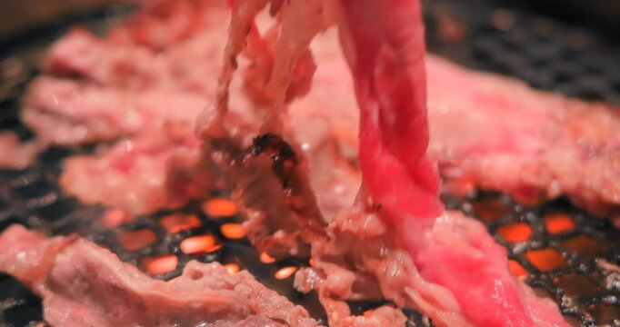網の上でトングを使って香ばしく焼き上げる大判の牛カルビ肉