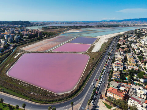 Aerial view of the pink salt pans of Cagliari, Sardinia, Italy, with colorful evaporation ponds beside the coastal road and city neighborhoods