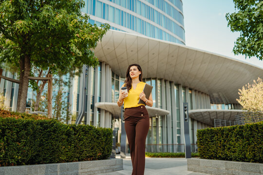 Woman walking business district holding coffee and tablet