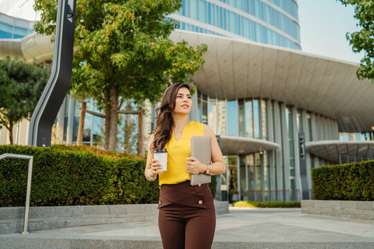 Professional businesswoman walking with coffee and laptop