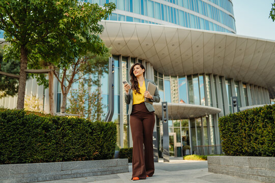 Businesswoman walking in city holding phone and laptop