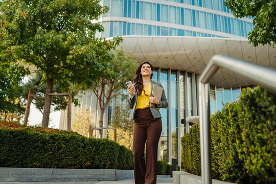 Businesswoman walking outdoors, carrying laptop and phone