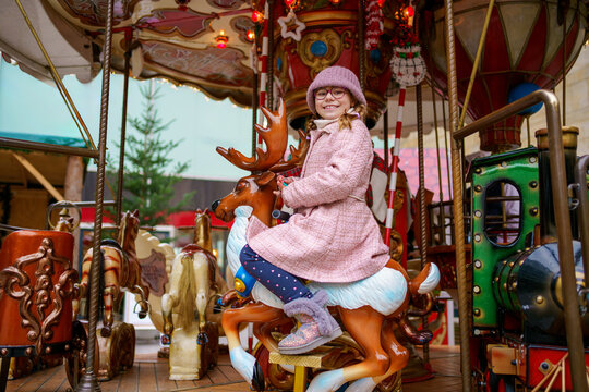 Little school girl riding on a merry go round carousel at Christmas funfair or market, outdoors. Happy child having fun on traditional family xmas market in Germany