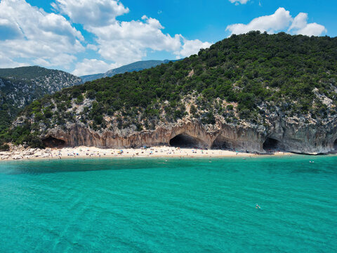 Cala Luna beach with caves, turquoise sea and green mountains under a blue sky with clouds, Gulf of Orosei, Sardinia, Italy