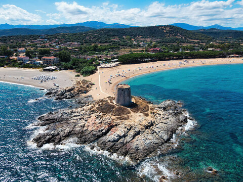 Aerial view of the Torre di Bari Sardo, an ancient watchtower on a rocky promontory, with sandy beach, turquoise sea and hills, Sardinia, Italy