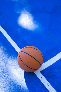 Orange basketball is resting on bright blue court near white lines with scuff marks, debris